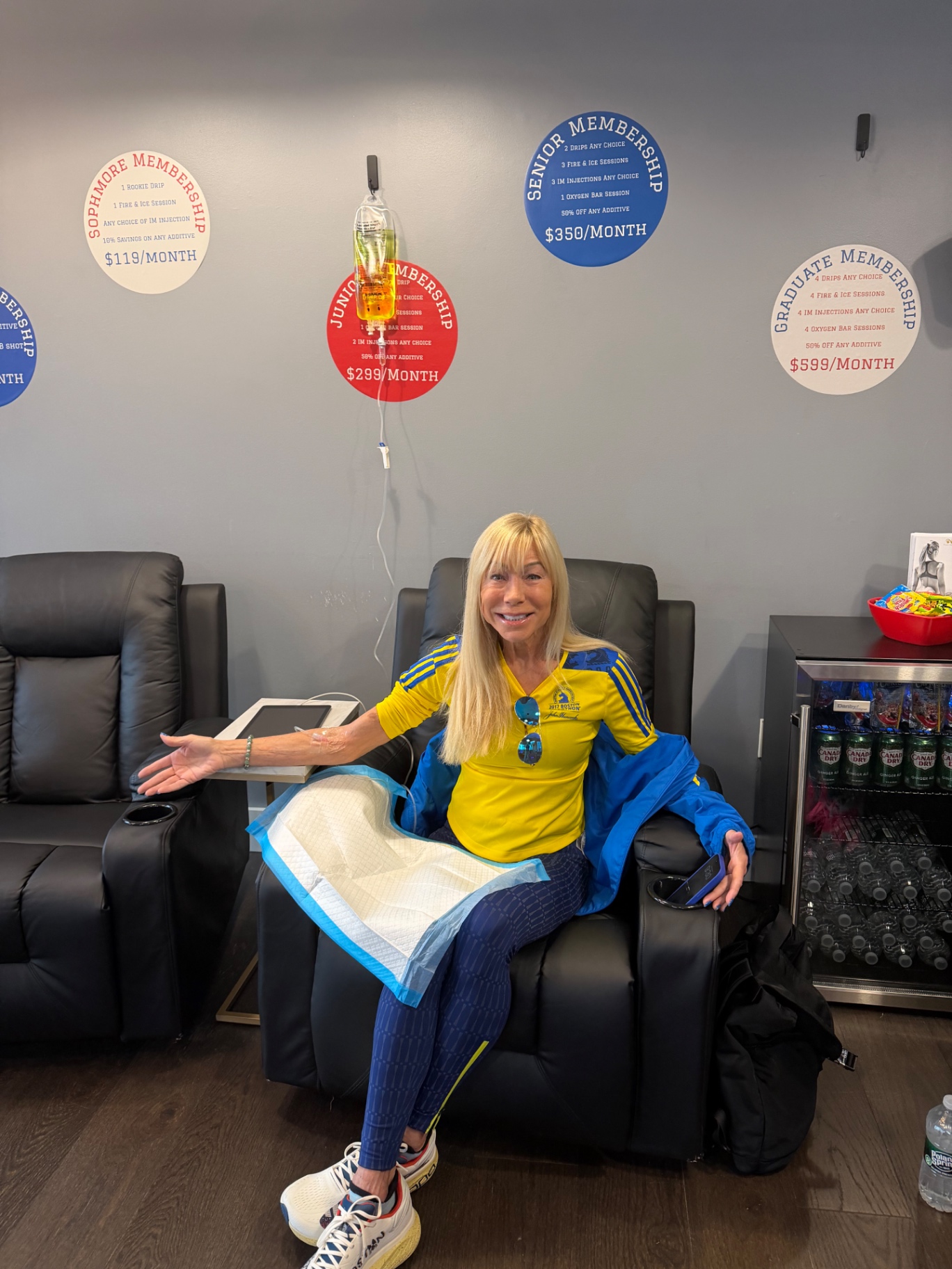 A Boston Marathon runner in a yellow and blue Adidas jacket relaxes in a recliner while receiving an IV drip inside the IV League Hydration lounge in South Boston