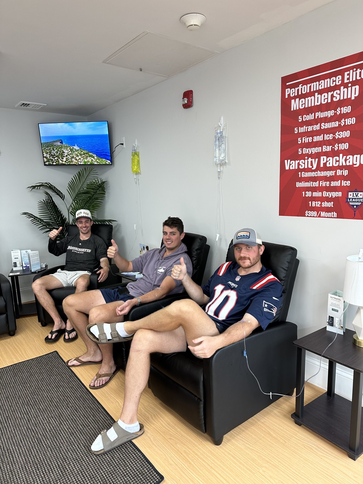 Clients in Boston sports jerseys relaxing during IV therapy beneath the Performance Elite membership sign