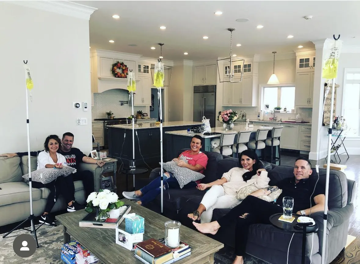 Couples and friends hydrating side by side with IV bags on stands in an open-concept home