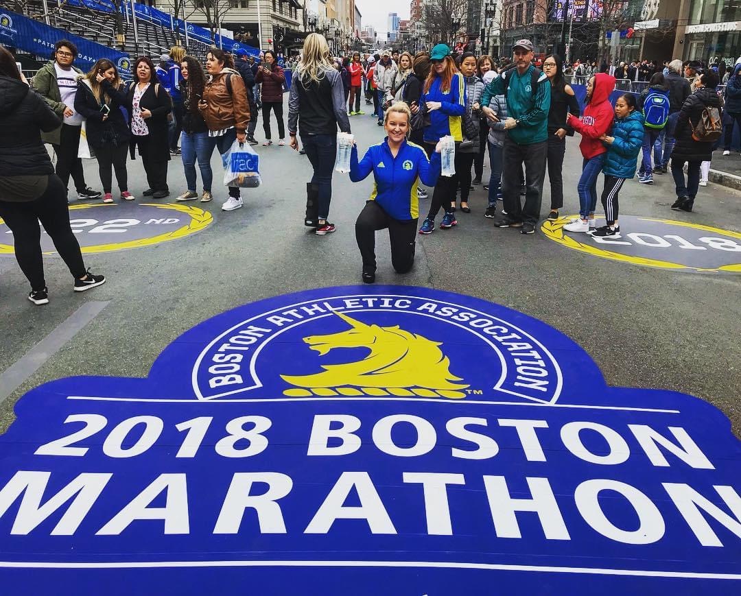 Courtney Jones, RN kneeling on the 2018 Boston Marathon finish line on Boylston Street holding water bottles