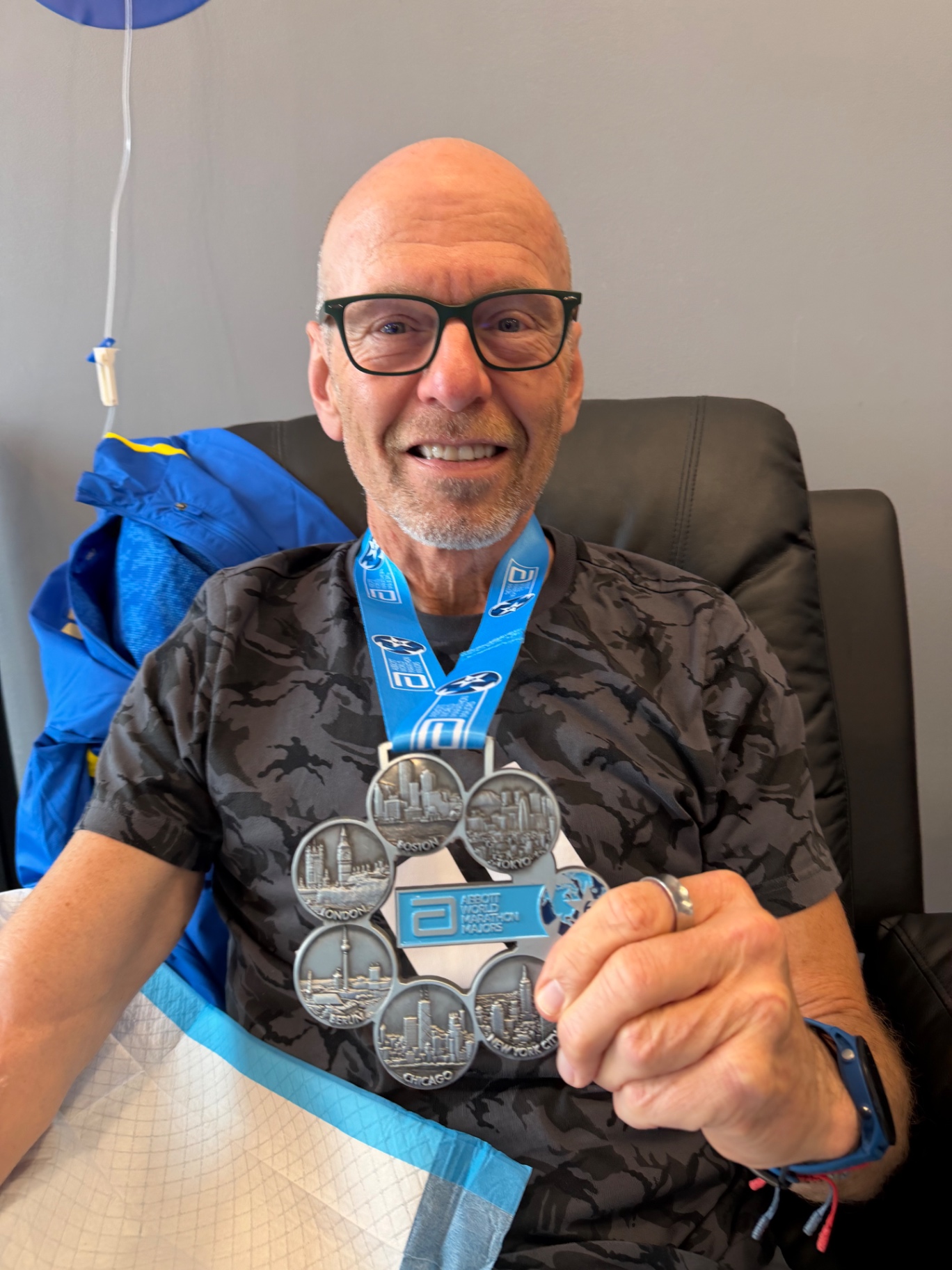 An Abbott World Marathon Majors Six Star finisher holds his medal while receiving an IV drip at IV League Hydration after the Boston Marathon