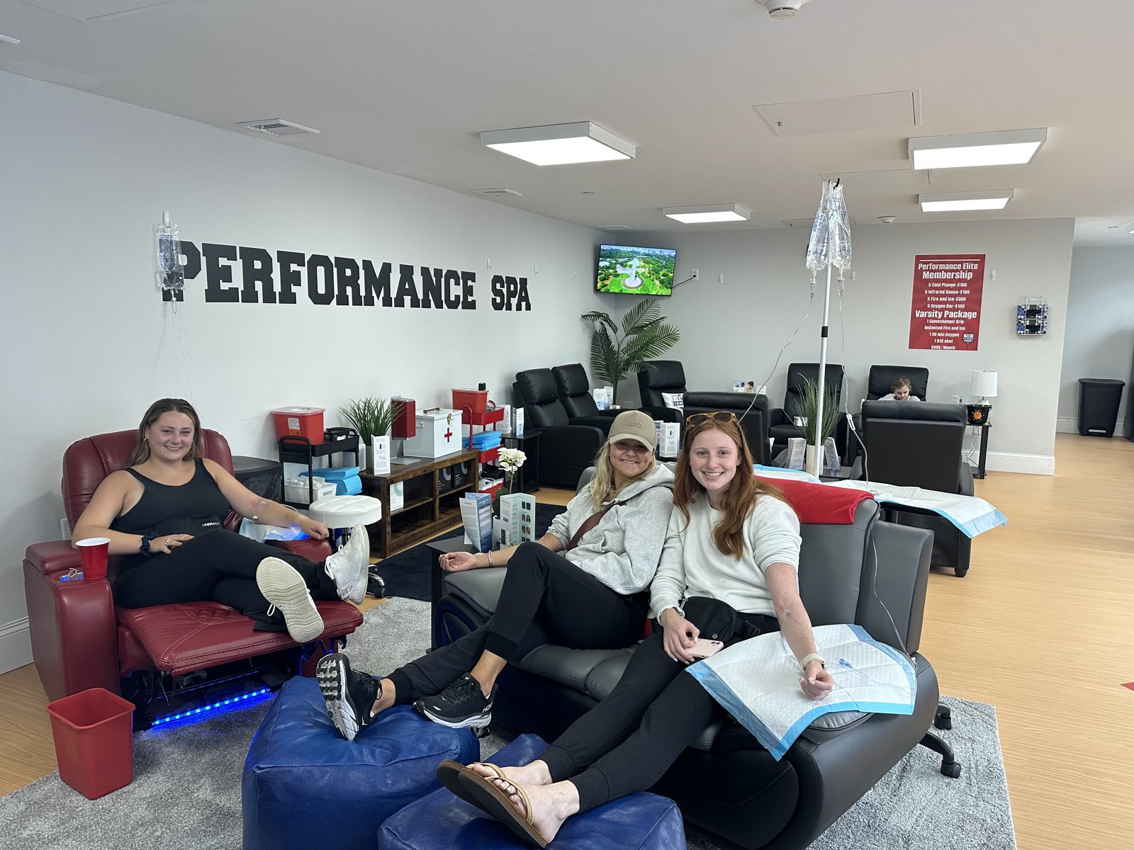 Friends receiving IV therapy together under the Performance Spa wall lettering at IV League Hydration