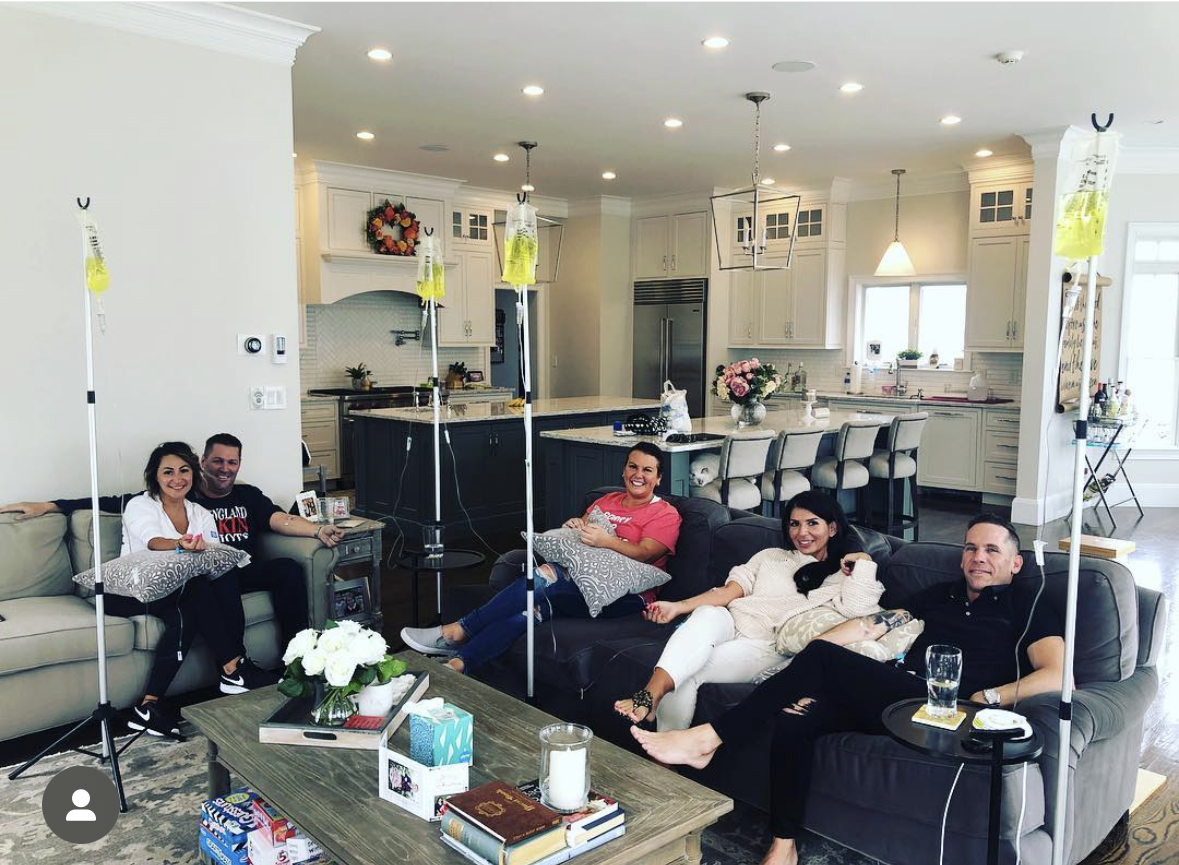 Couples and friends hydrating side by side with IV bags on stands in an open-concept home